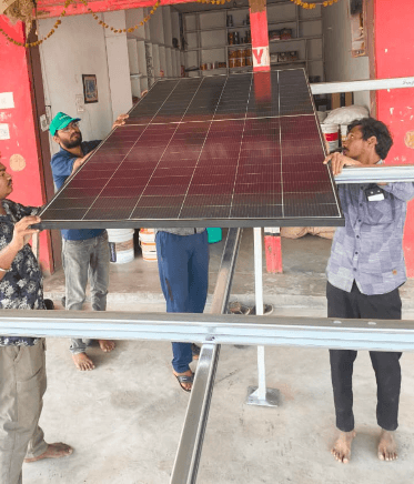 A technician fitting a solar inverter to the wall of a building while standing on a step ladder